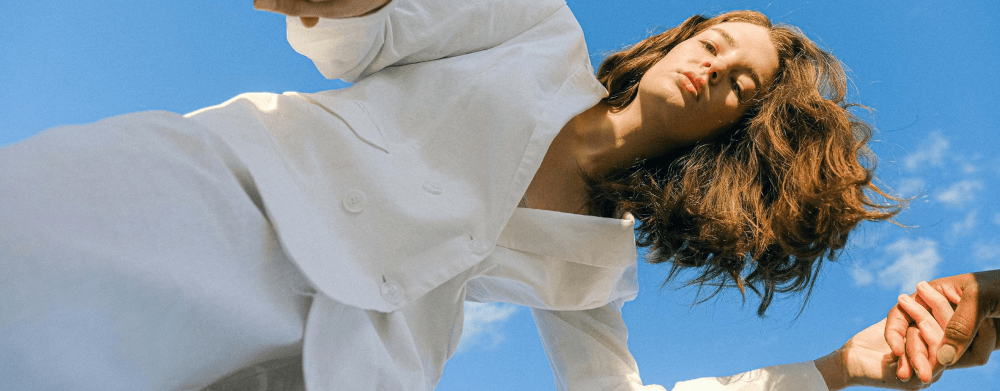 Woman leaning back joyfully against a blue sky, reaching out a hand