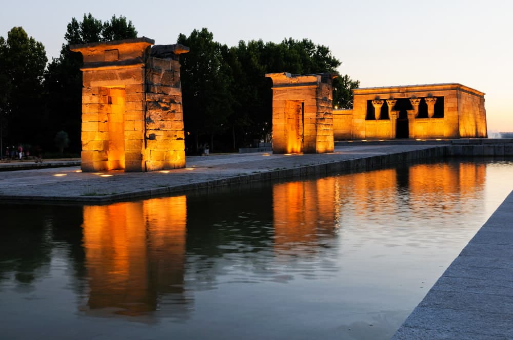 Ancient Temple of Debod illuminated at sunset in Madrid's Parque del Oeste, Egyptian temple relocated to Spain with golden stone architecture reflecting in water, historic landmark with original 4th century BCE Nubian design