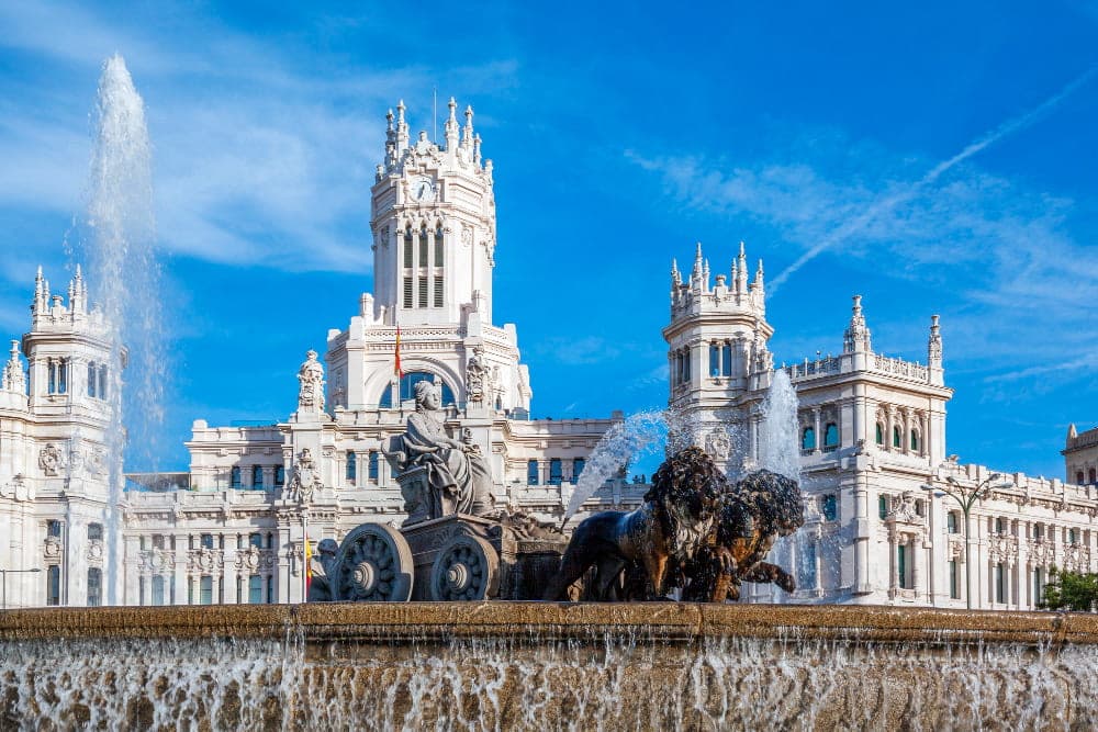 Cibeles Fountain in Madrid with white marble neoclassical sculpture of goddess Cybele riding lion-drawn chariot against blue sky, iconic Spanish landmark and celebration site for Real Madrid victories
