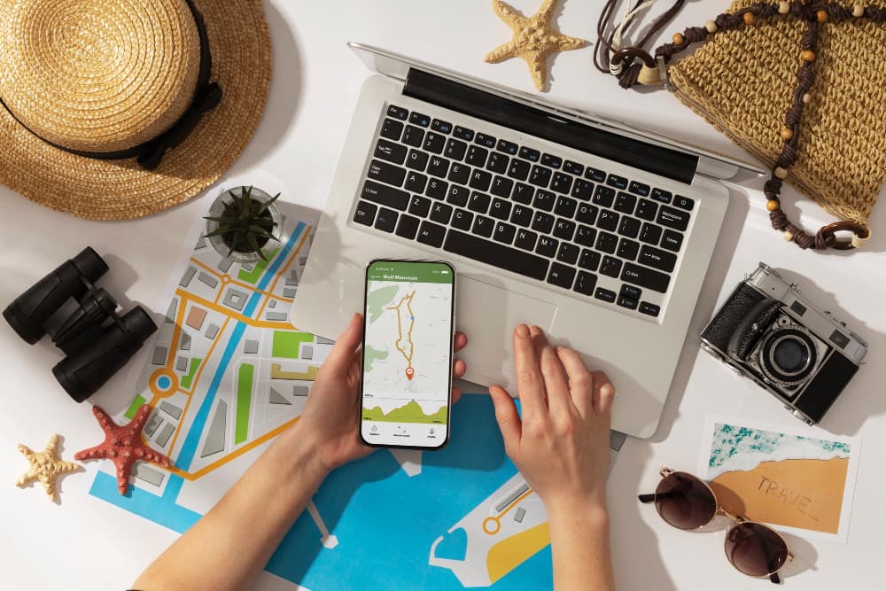 Phone showing a maps app beside travel essentials and a laptop