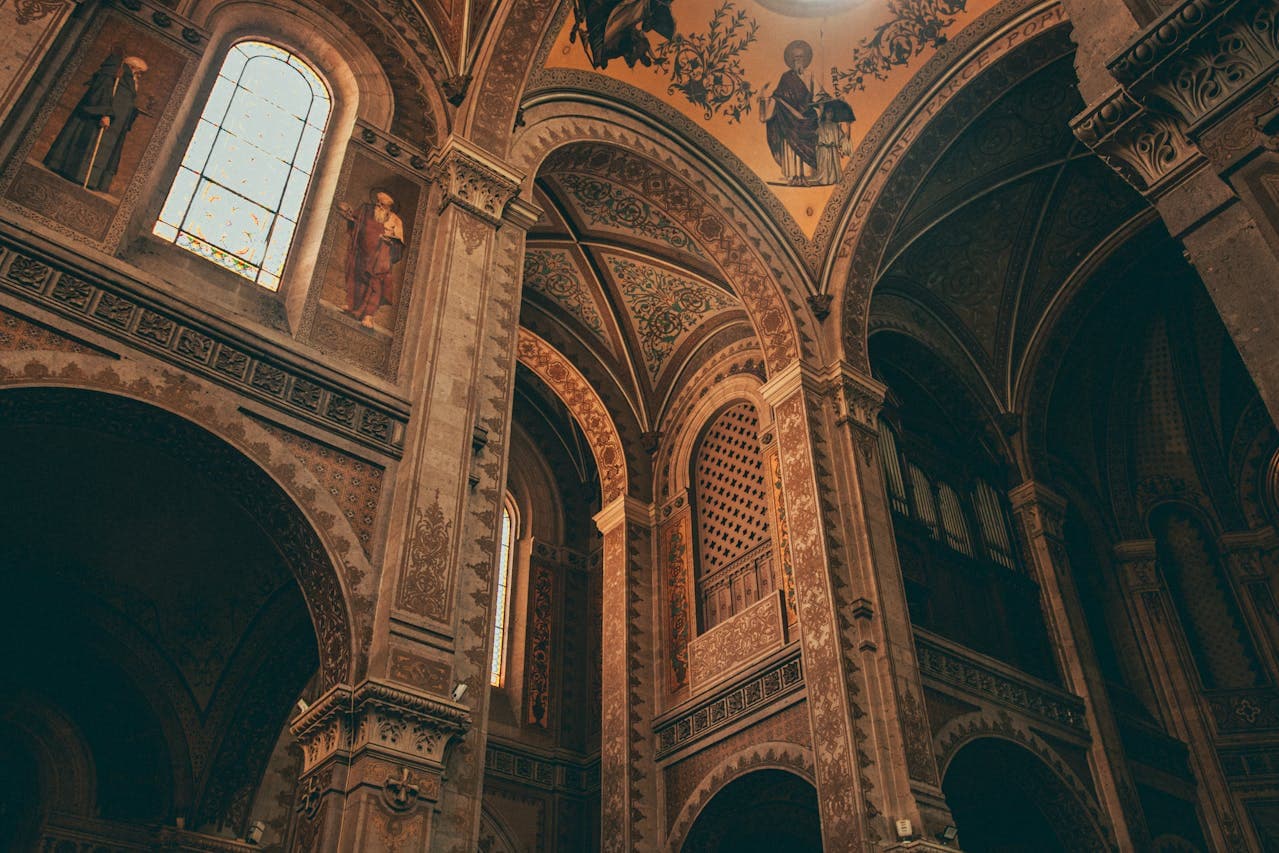Ornate church interior featuring vaulted arches, intricately painted columns, frescoed ceilings, and a stained‑glass window filtering soft light.