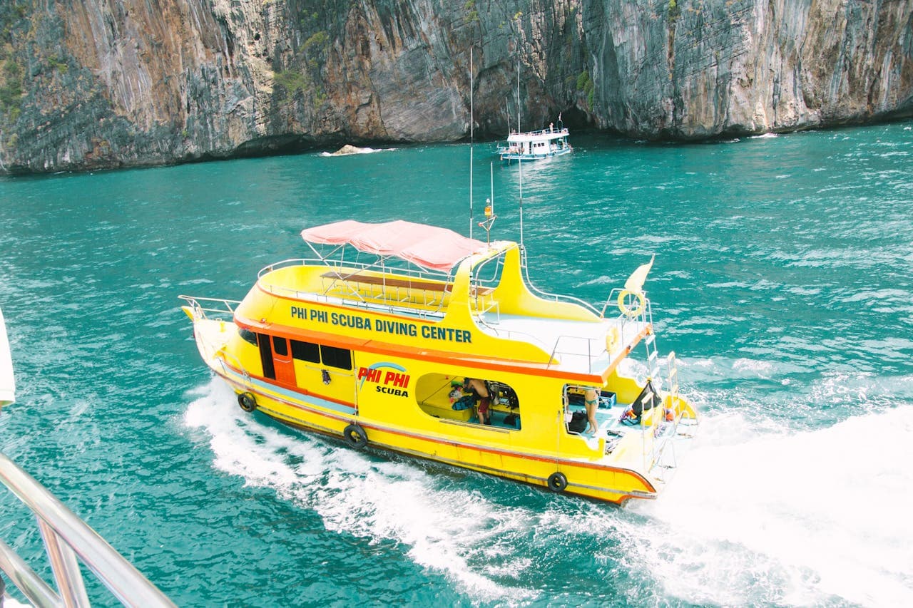 Yellow Phi Phi Scuba Diving Center boat cruising in emerald waters near rocky cliffs in Thailand