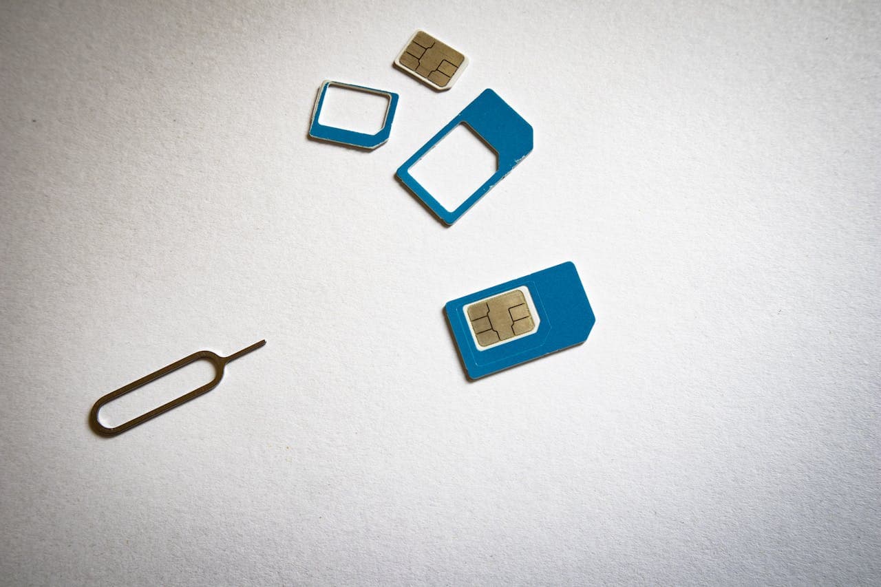 SIM card with blue adapter frames and a SIM ejector tool on a white surface.