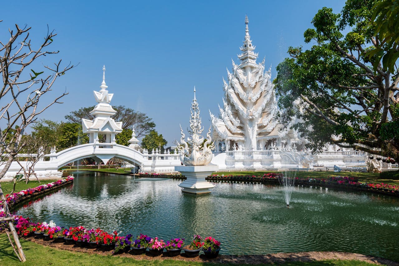 White Temple Wat Rong Khun in Chiang Rai, Thailand with ornamental pond and gardens under clear blue sky