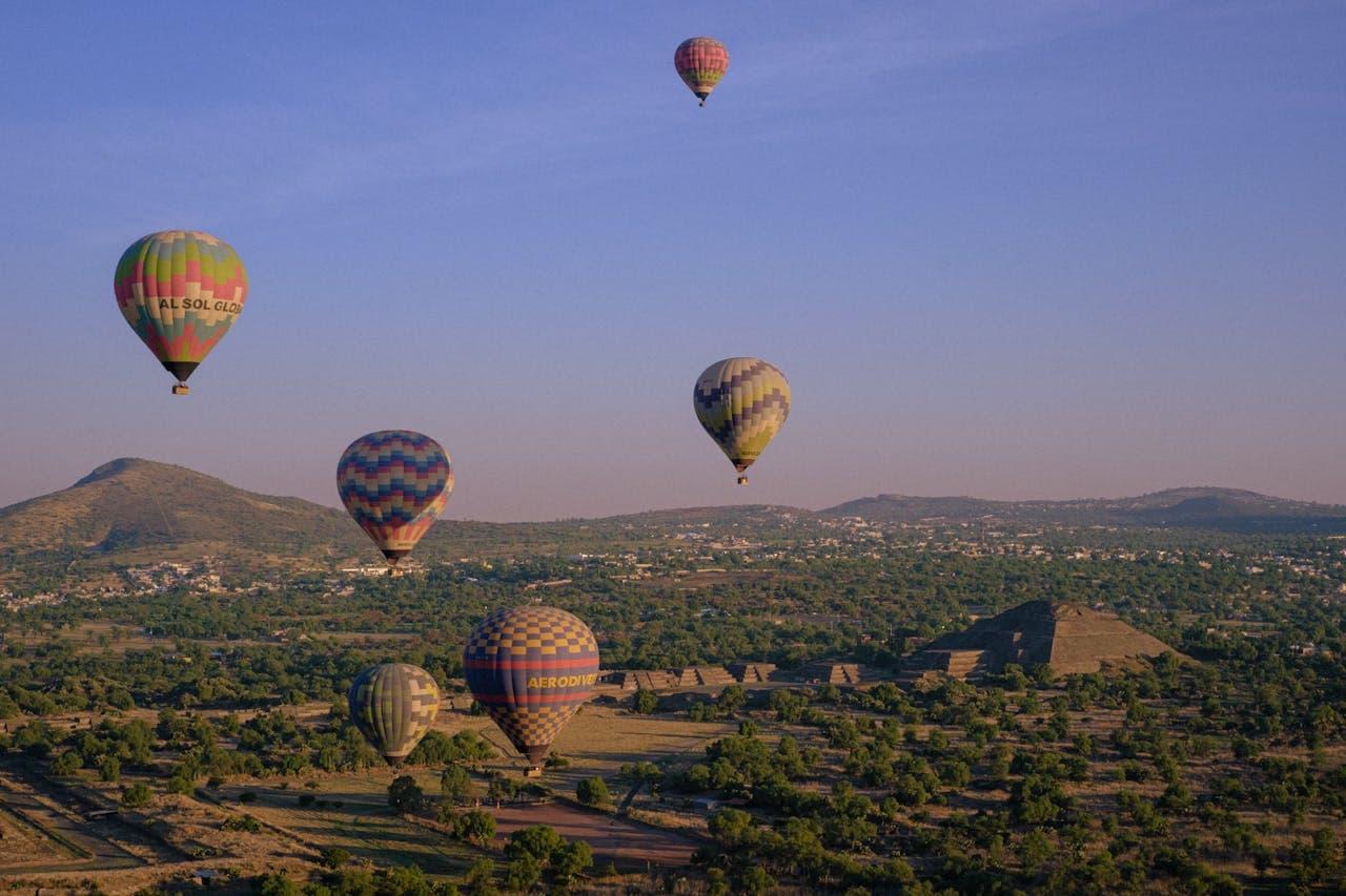 Colorful hot air balloons drifting over the Pyramid of the Sun and Pyramid of the Moon at the ancient Teotihuacán archaeological site during sunrise.