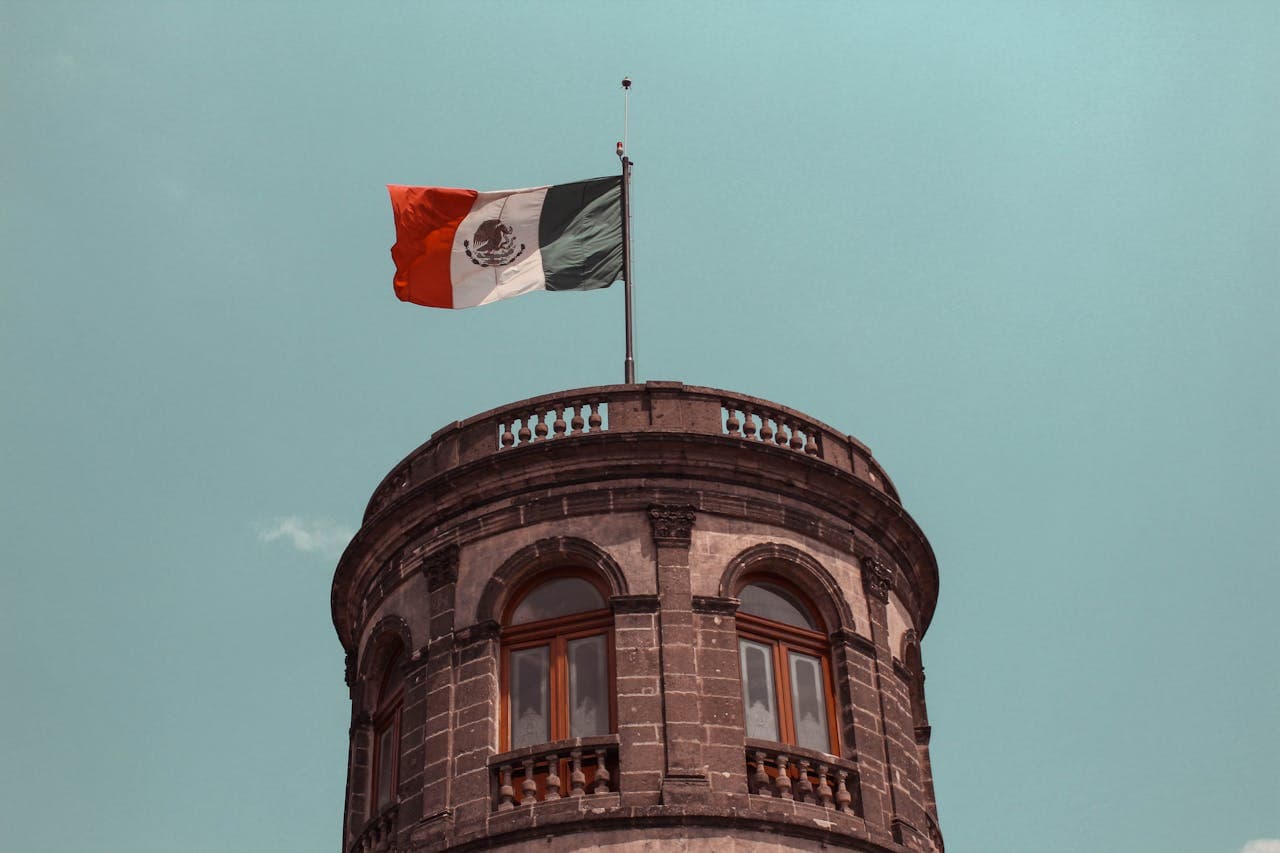 Historic stone tower with arched windows displaying the Mexican flag waving under a clear sky