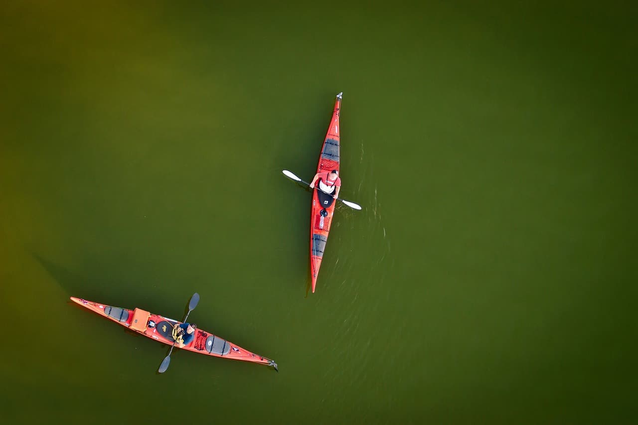 Aerial view of two people kayaking in red kayaks on calm green water, showcasing outdoor adventure and water sports.