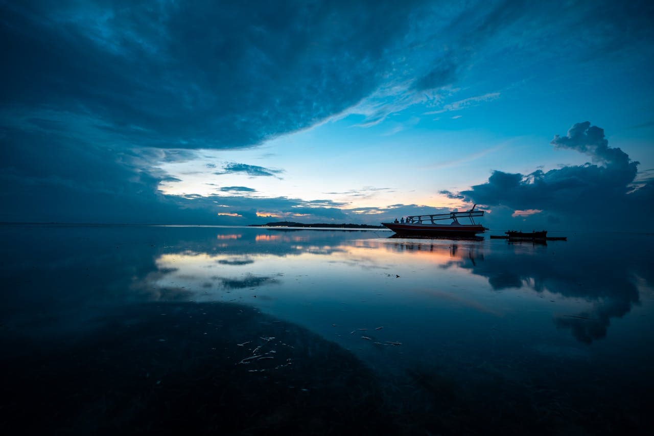 Fishing boat silhouetted on calm water at dusk in Bali