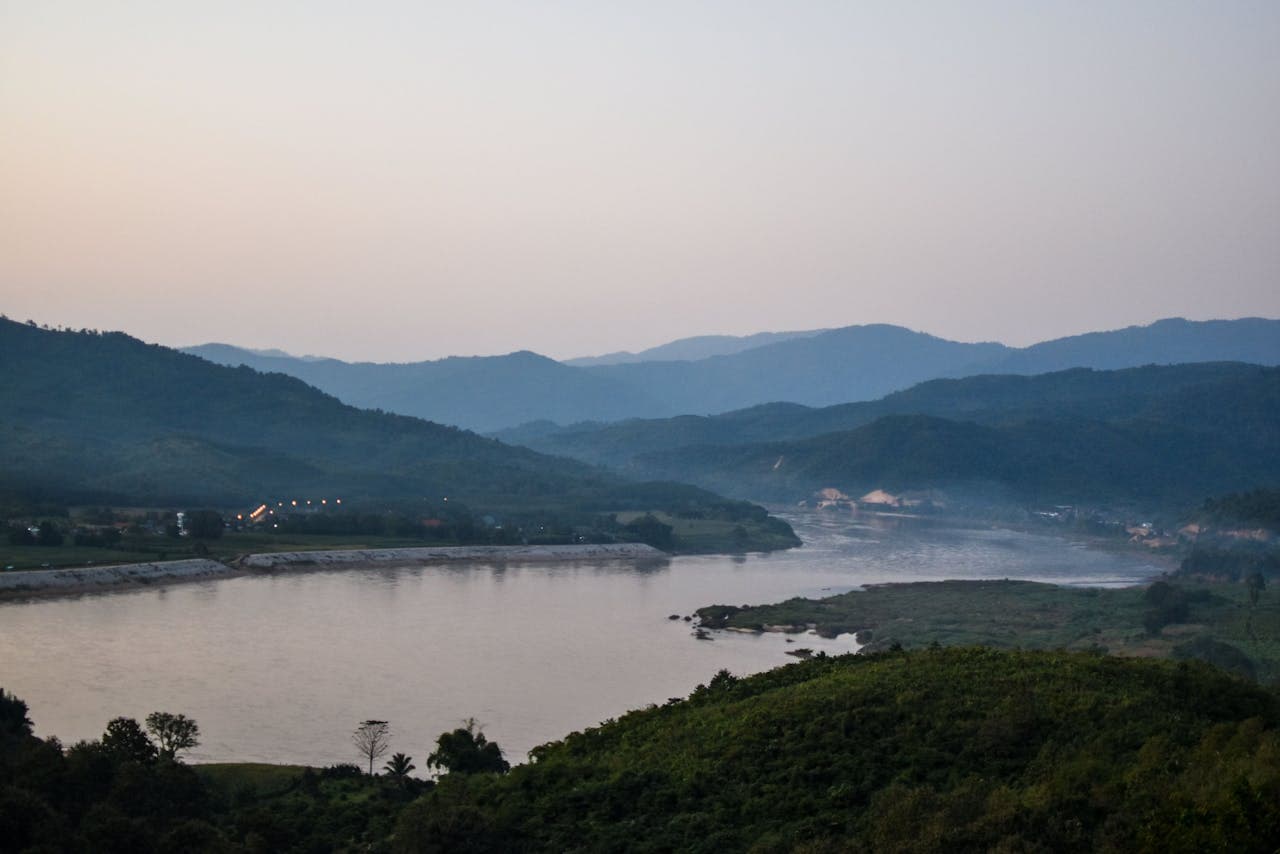 Panoramic view of a tranquil river winding through lush green mountains under a pastel sunset sky