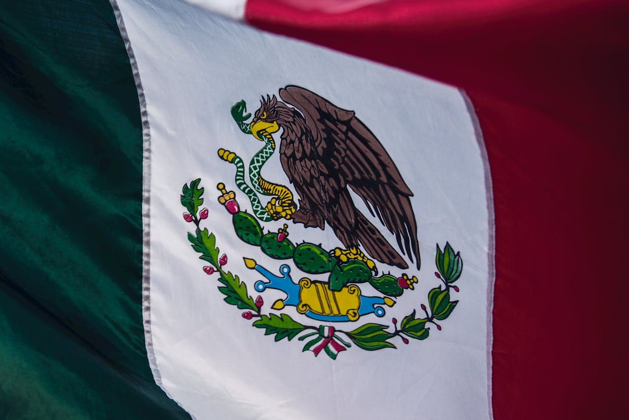 Close-up of the Mexican flag featuring the national emblem of an eagle with a snake in its beak perched on a cactus.