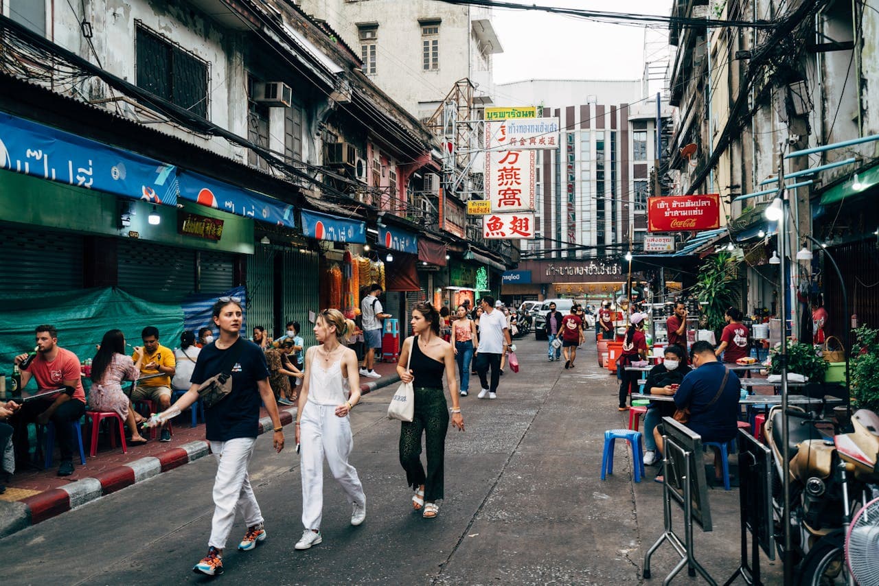 Busy Bangkok street food market with pedestrians, outdoor vendors under colorful neon signs and Thai shopfronts