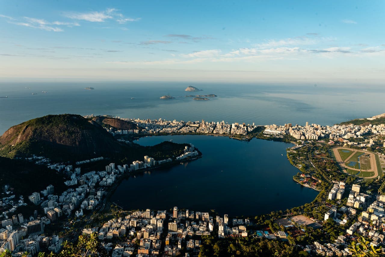Panoramic view of Rio de Janeiro featuring the Rodrigo de Freitas Lagoon, surrounding cityscape, forested hills, and the Atlantic Ocean with distant islands.