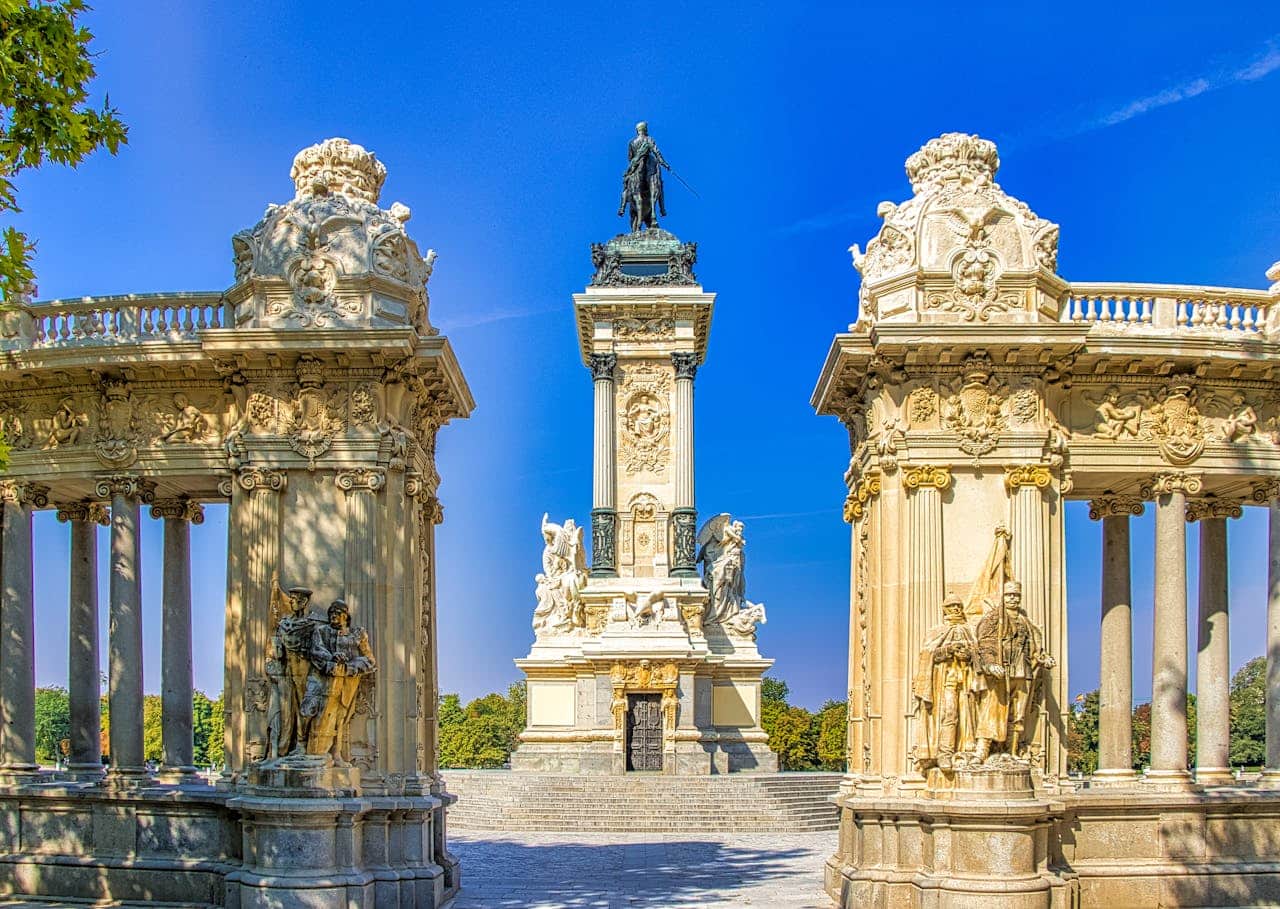 Monument to King Alfonso XII with ornate columns and statues in Retiro Park, Madrid, under a clear blue sky.