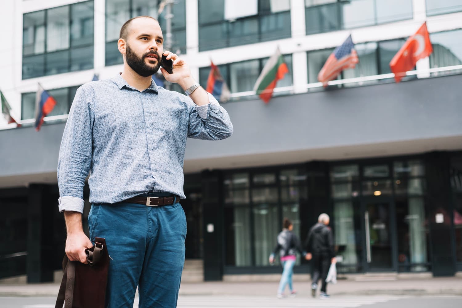 Man making an international call outside a building flying flags from different countries