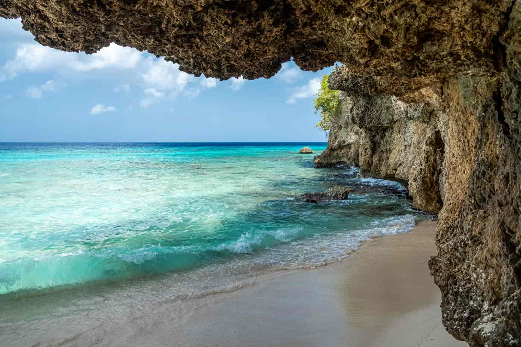 Turquoise waves gently lap against a sandy shore, framed by rugged coastal cliffs under a clear blue sky.