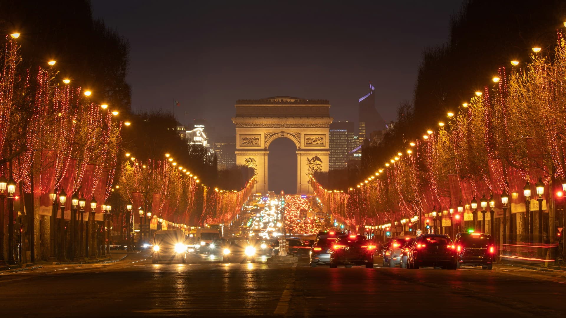 The Arc de Triomphe at night, with the Champs-Élysées illuminated by streetlights and car headlights, creating a vibrant city scene.