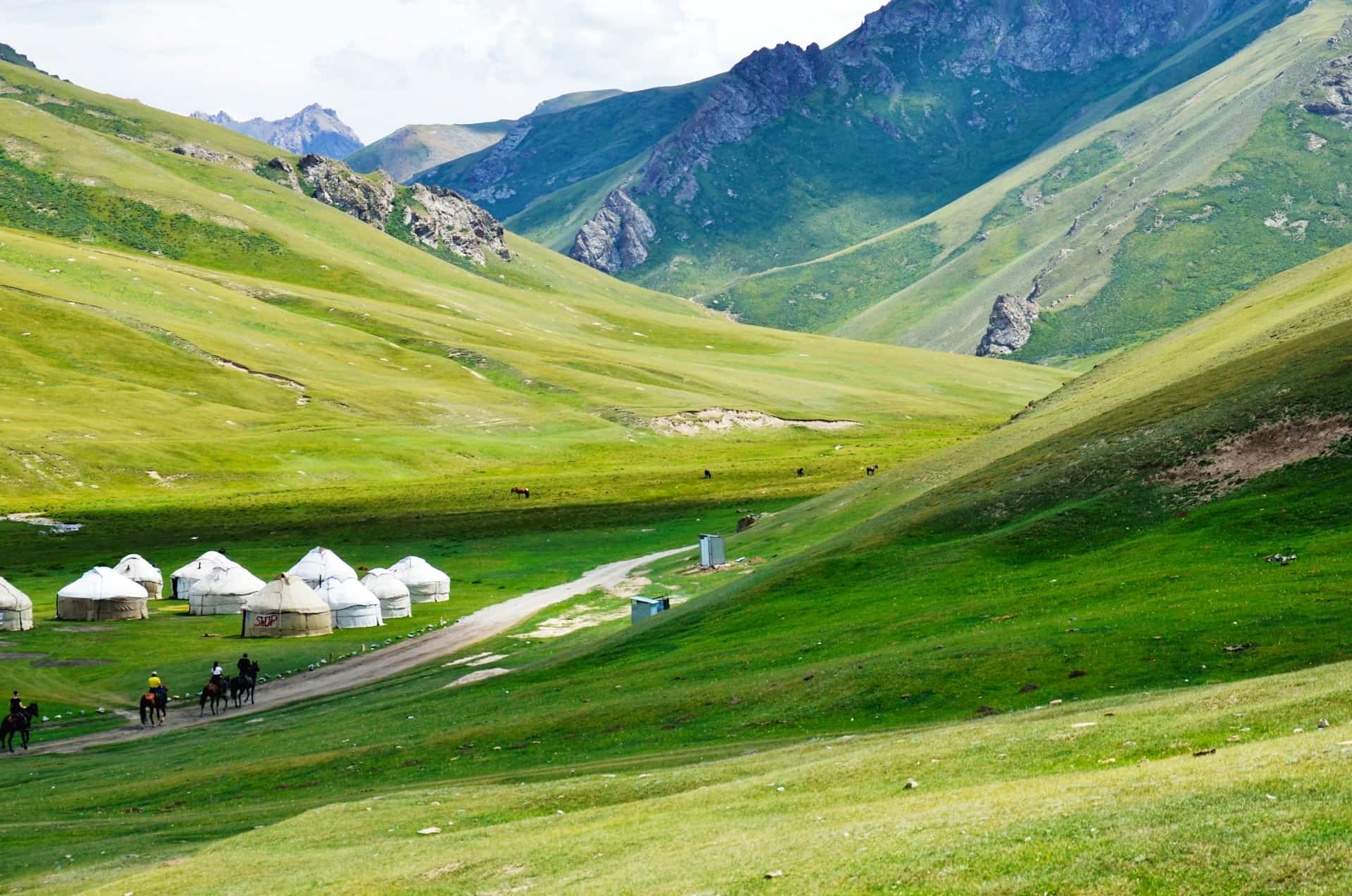 Yurts and horse riders in a green Kyrgyzstan mountain valley