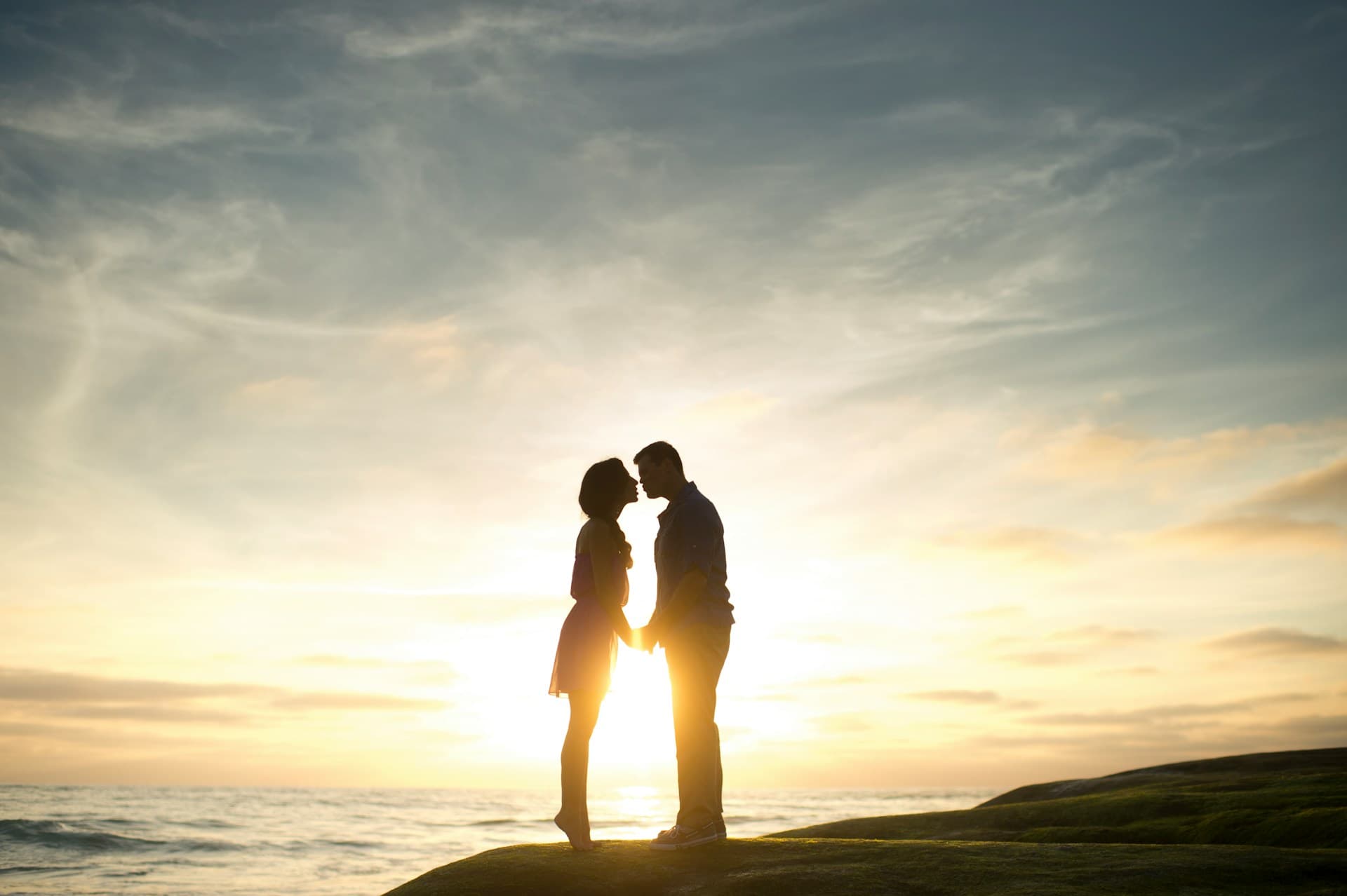 Silhouetted couple embracing at sunset on a coastal cliff