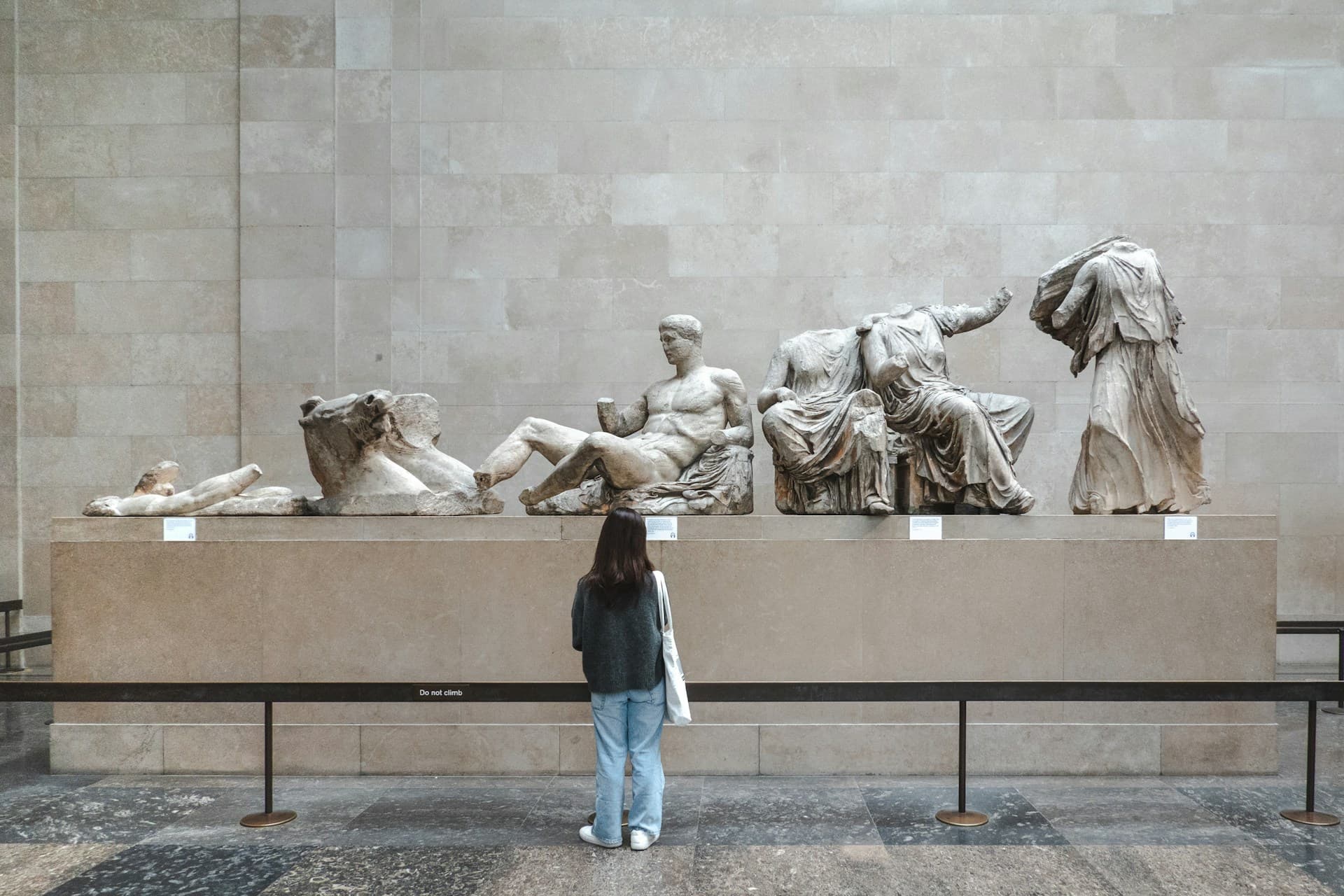 Visitor viewing ancient Greek marble sculptures of reclining and draped figures in a museum.