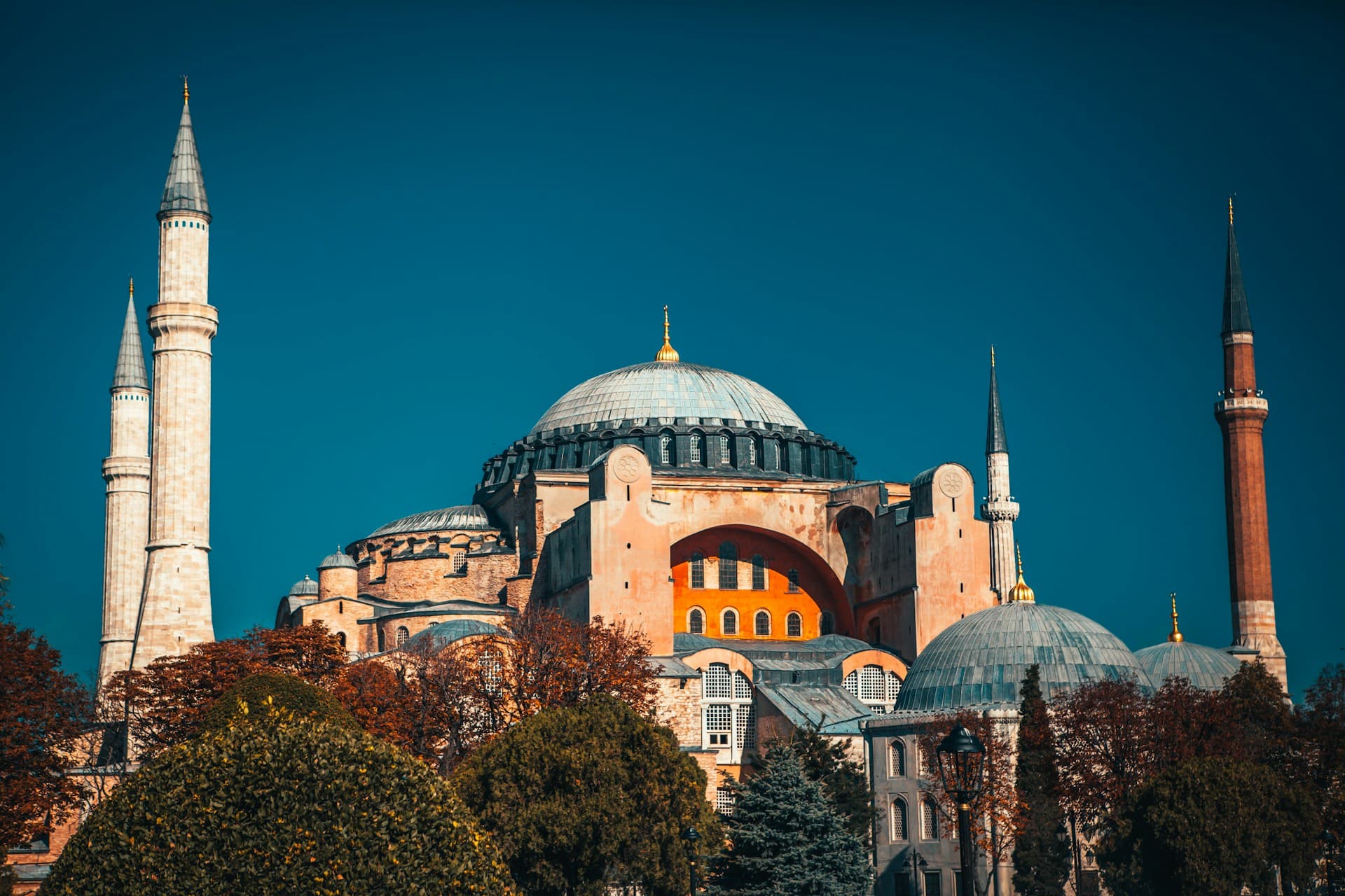 Hagia Sophia in Istanbul with central dome and four minarets rising above trees against a deep blue sky