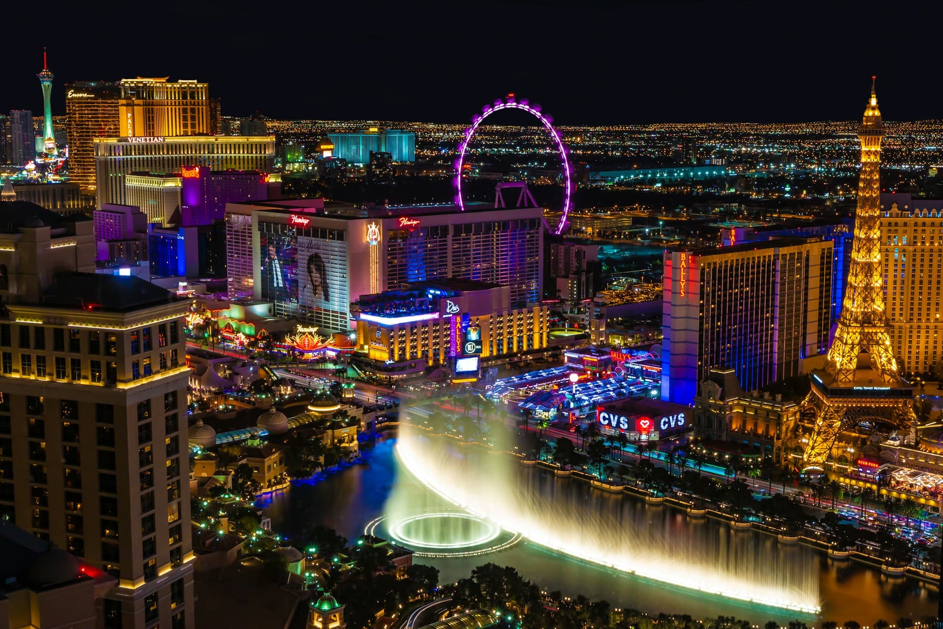 Aerial view of the Las Vegas Strip at night, featuring bright lights, the High Roller Ferris wheel, and the Bellagio fountains.