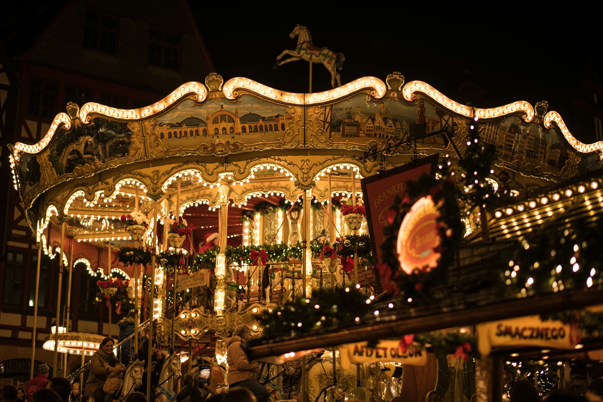 Illuminated vintage carousel at night, adorned with festive lights and garlands, featuring a horse figure on top.