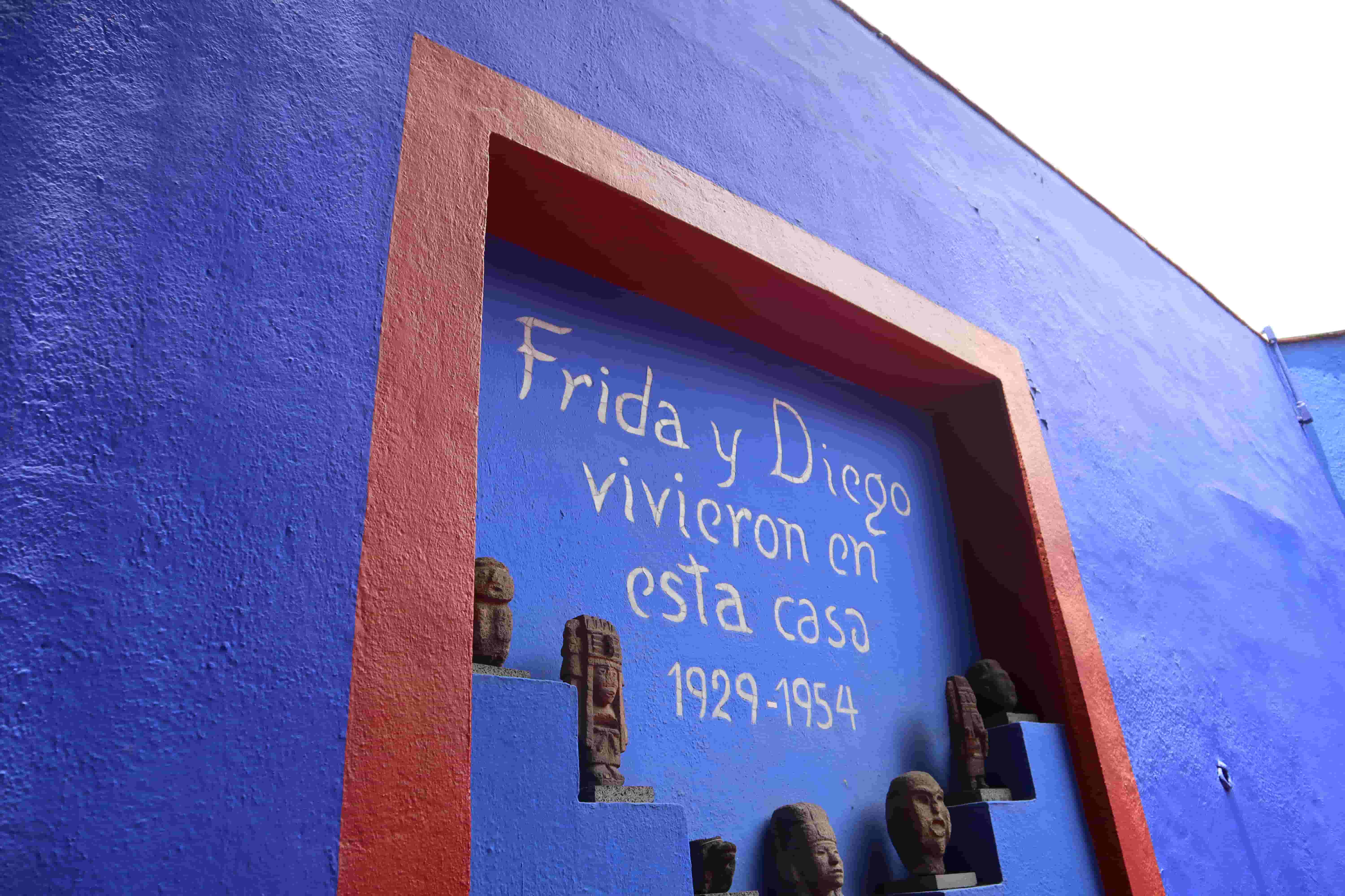 Blue exterior wall of Frida Kahlo and Diego Rivera's house with red trim and traditional Mexican sculptures