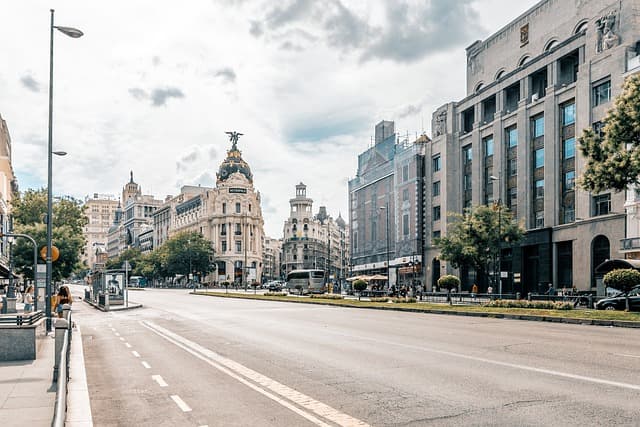 Wide-angle view of Gran Via street in Madrid featuring the iconic Metropolis Building and historic architecture on a bright, partly cloudy day.