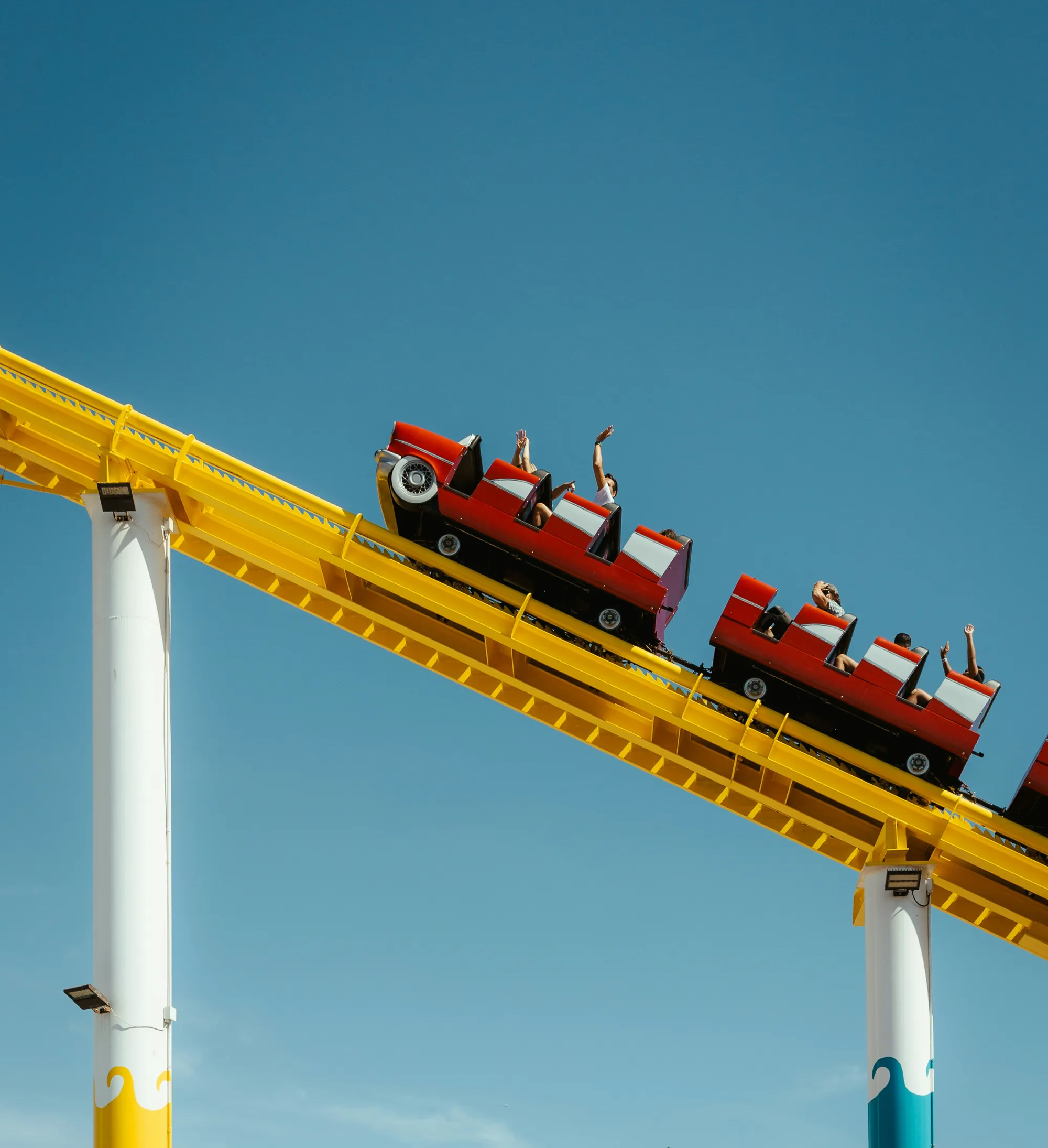 A red roller coaster heading down a yellow track, riders with their arms up