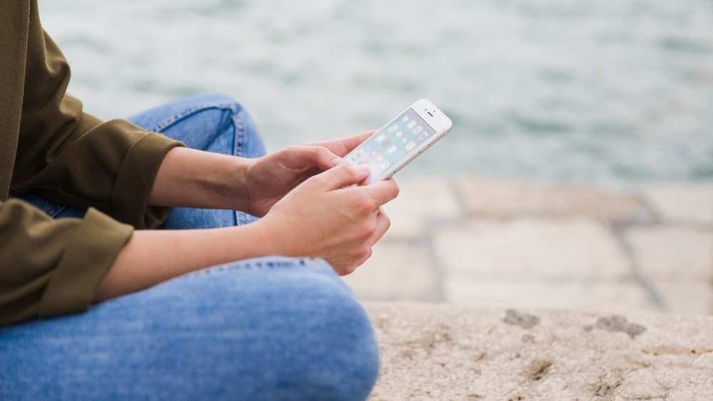 Person sitting by the water using a phone