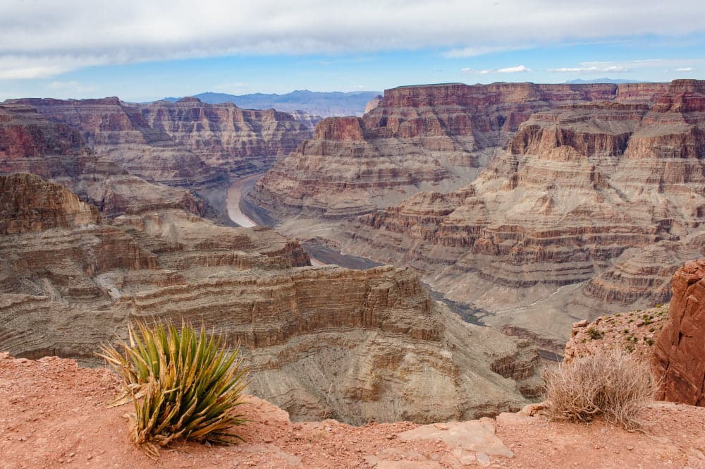 Panoramic view of the Grand Canyon with layered rock formations and a river below.