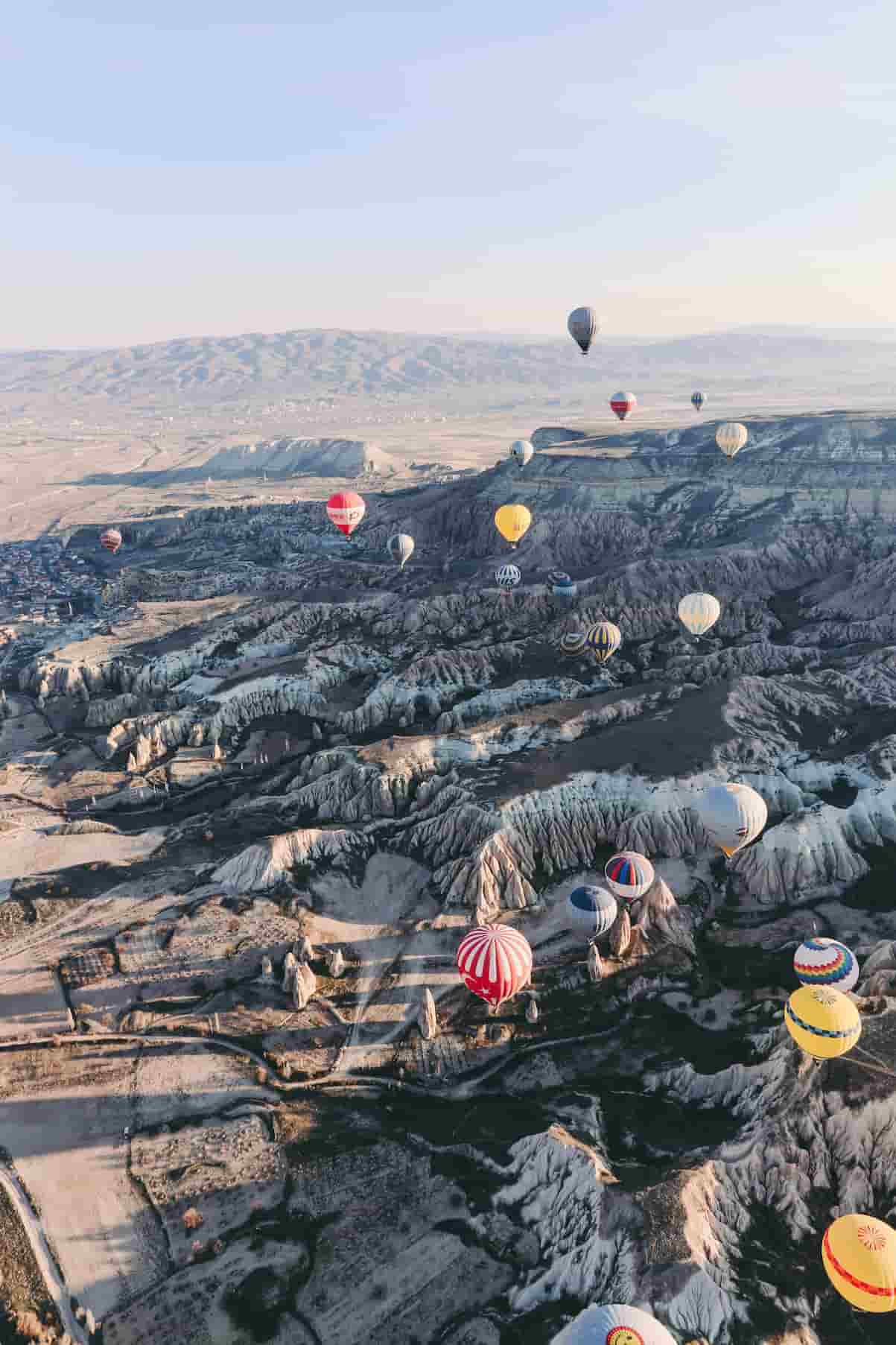 Hot air balloons floating over a rocky landscape with rolling hills, under a clear blue sky.