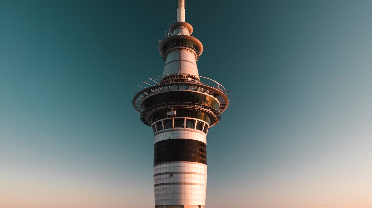 Close-up view of a modern telecommunications tower against a clear blue sky at sunset, highlighting its architectural details and observation deck