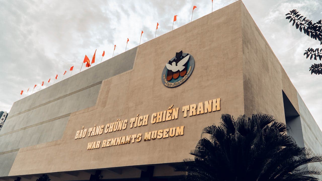 Exterior view of the War Remnants Museum in Ho Chi Minh City, Vietnam, with Vietnamese flags on the rooftop and the museum's name in both Vietnamese and English.
