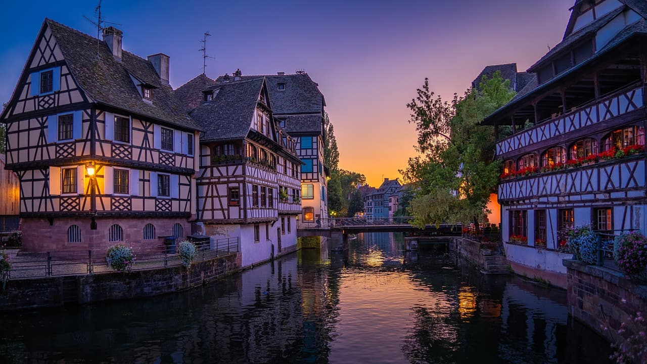 Charming canal with half-timbered houses at sunset, reflecting in the water, surrounded by lush greenery and a vibrant sky.