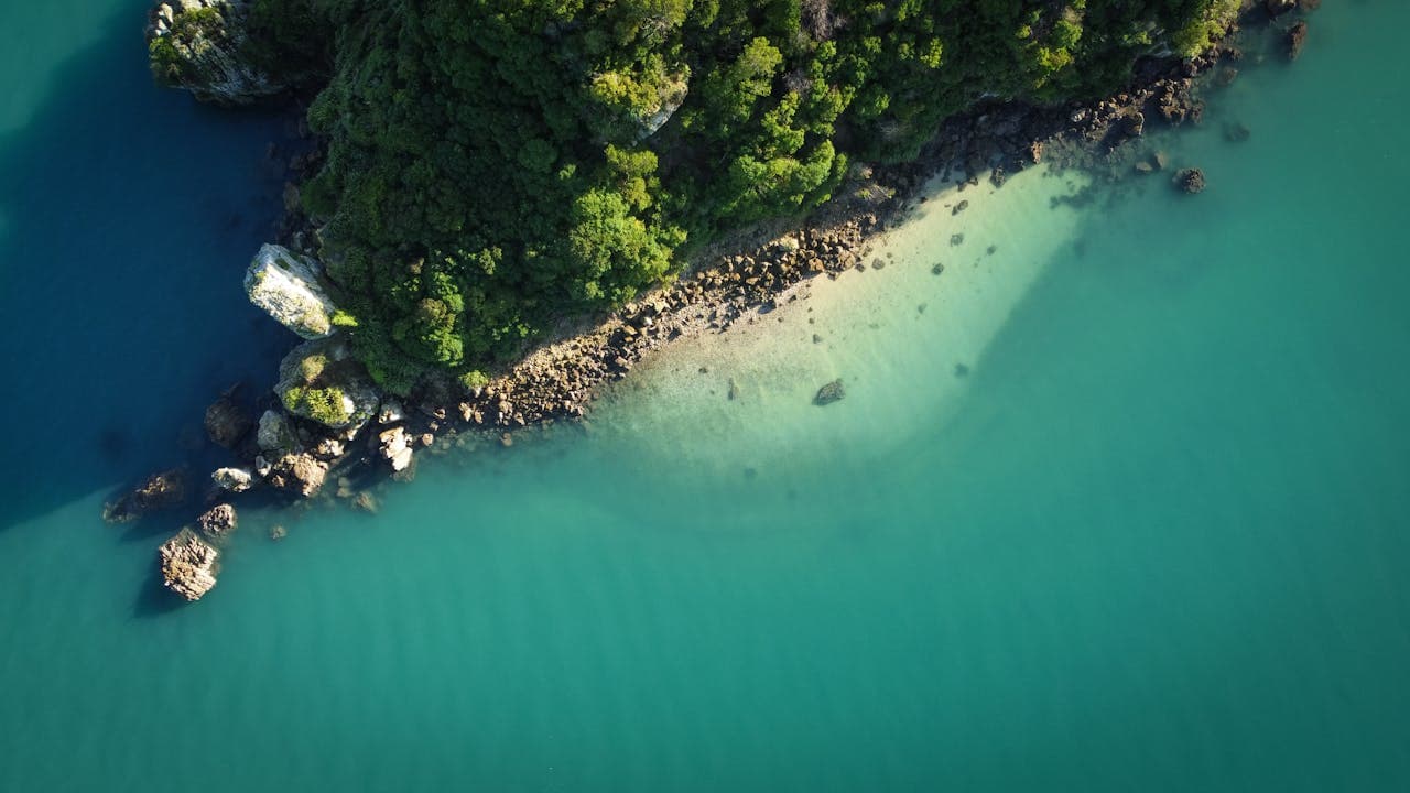 Aerial view of a lush green coastline with rocky outcrops and turquoise water, showcasing natural beauty and clear coastal waters.