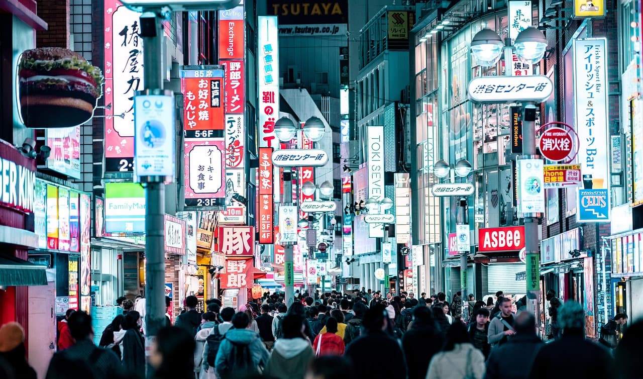 Bustling Tokyo shopping street at night, neon-lit signs and billboards in Japanese towering over a crowded pedestrian avenue.