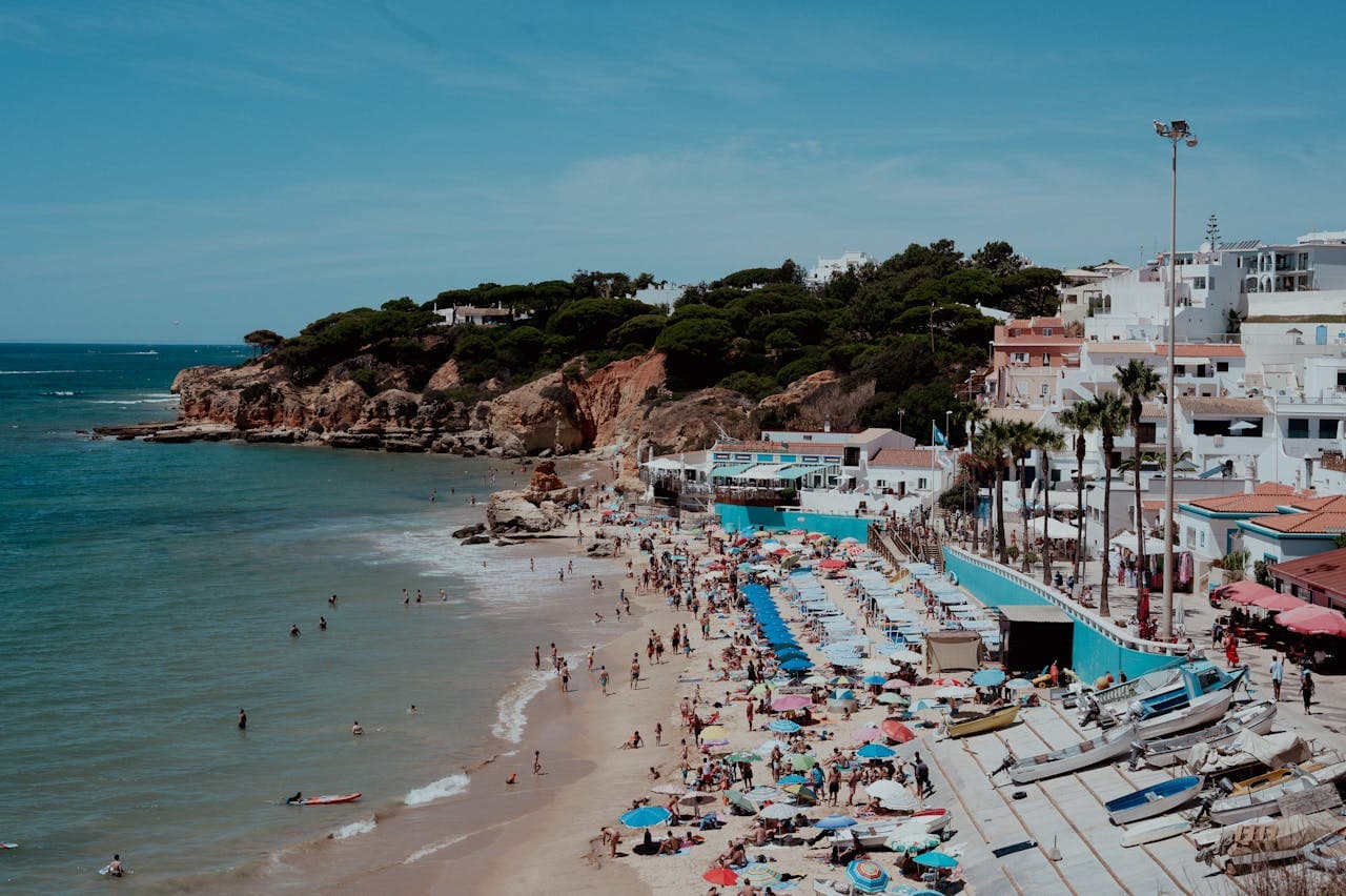 Beach in Albufeira packed with people, sun beds and parasol umbrellas in front of white coloured buildings.