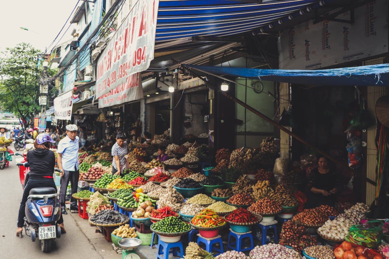 Outdoor Vietnamese street market with colorful fresh vegetables and spices displayed in baskets along a busy sidewalk