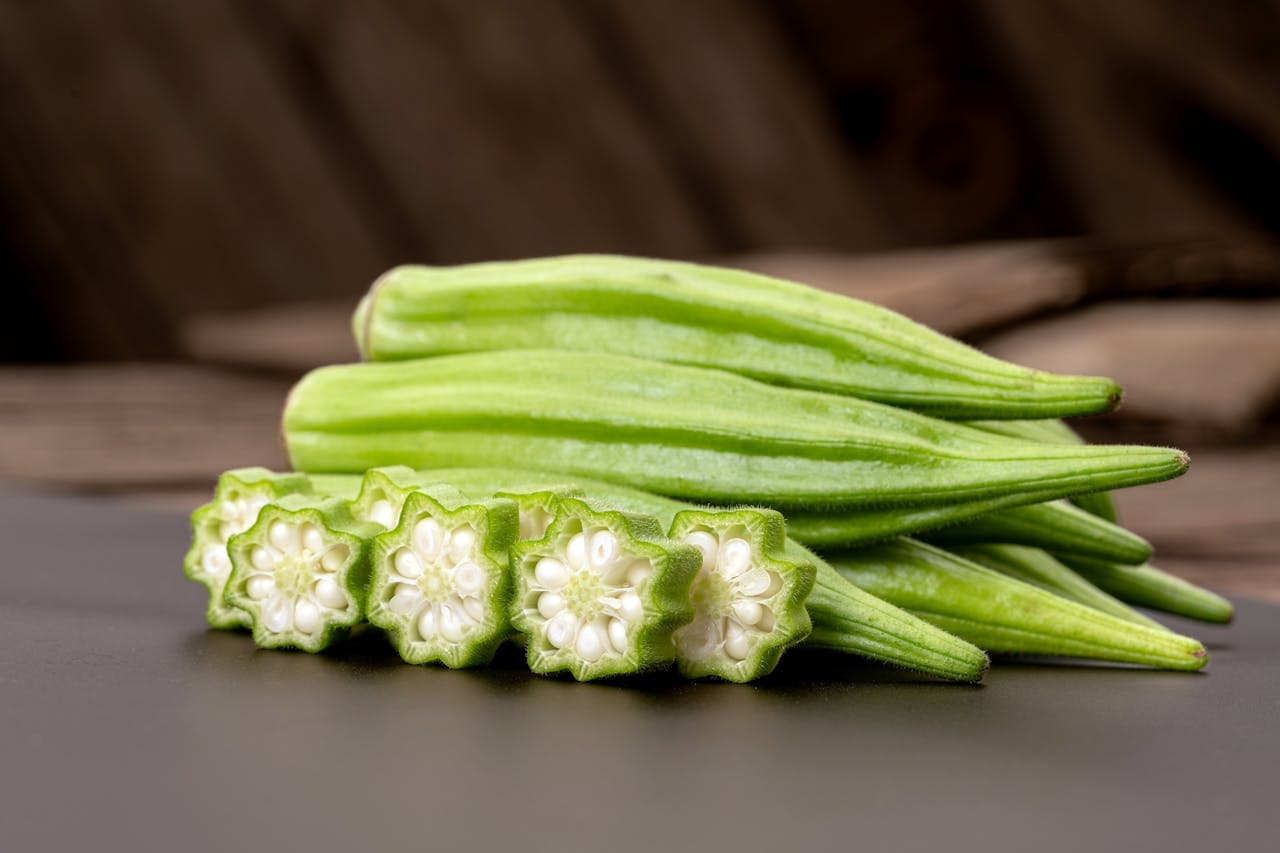 Fresh green okra pods with cross-section slices showing seeds on a dark surface, ideal for healthy cooking and vegetable recipes.