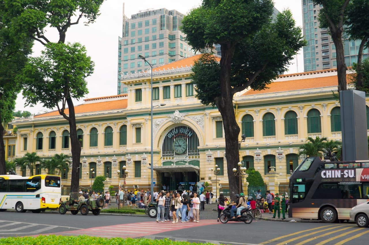 Exterior view of the Saigon Central Post Office in Ho Chi Minh City, Vietnam, with tourists and buses in front of the historic French colonial building.