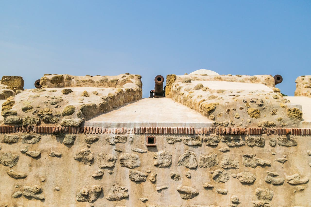 Ancient stone fort wall with mounted cannons under a clear blue sky, showcasing historic military architecture.