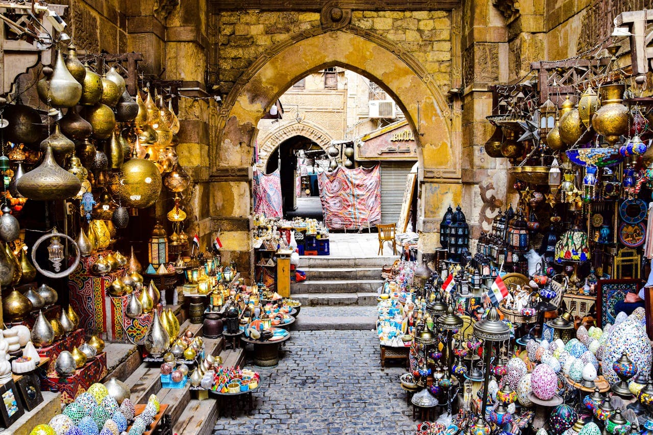 Traditional Middle Eastern bazaar with colorful lamps, brassware, and handicrafts displayed under a historic stone archway.