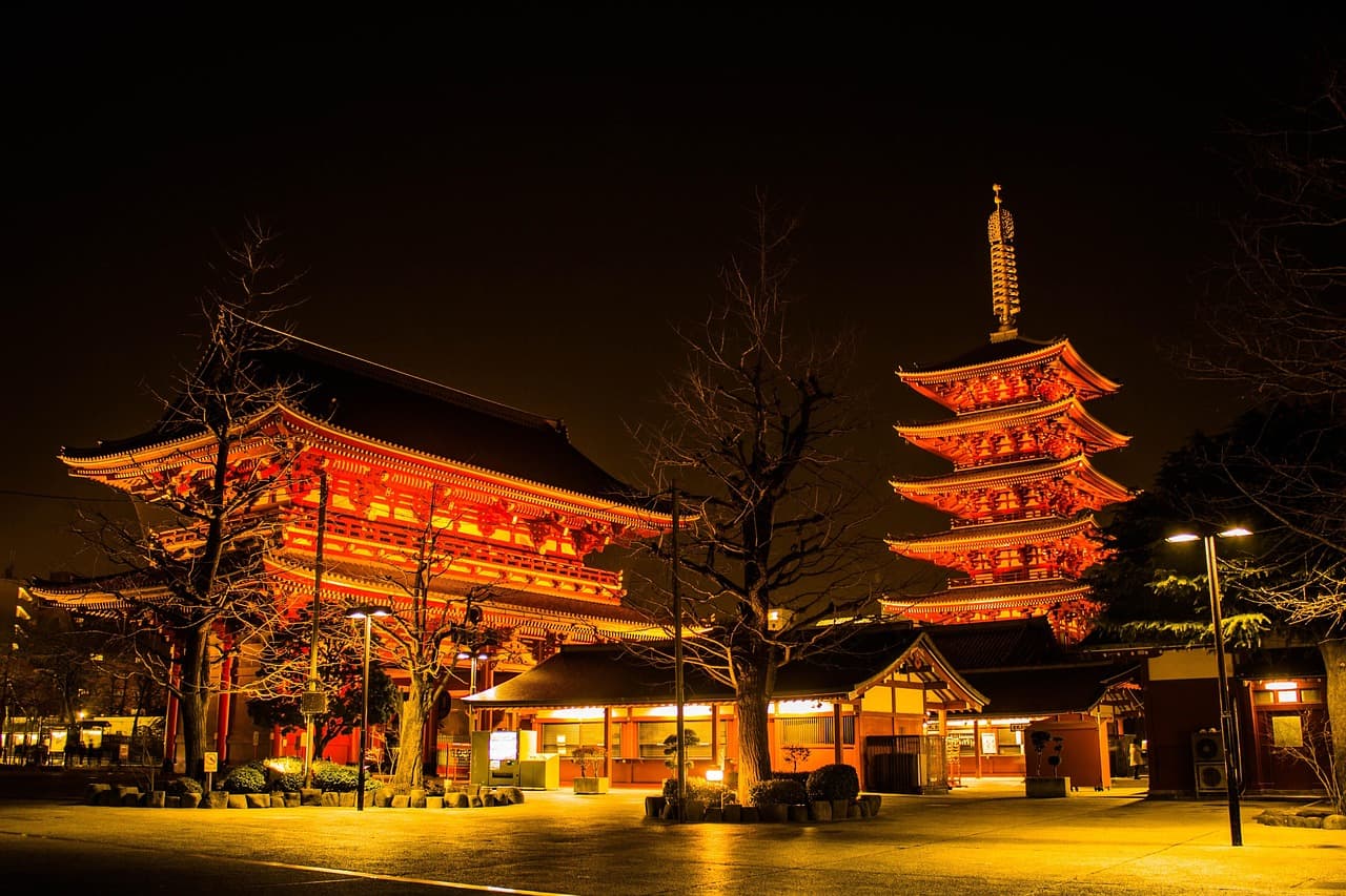 Illuminated red temple gate and five-story pagoda glowing at night in an empty courtyard
