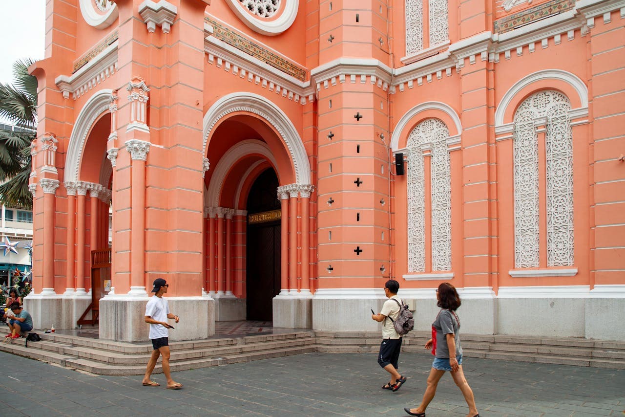 Tourists walking by the vibrant pink facade of Tan Dinh Church with intricate white detailing in Ho Chi Minh City, Vietnam