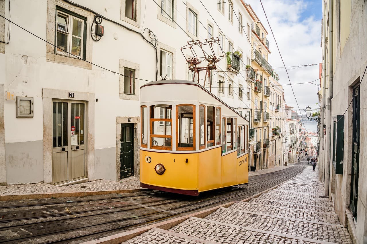 Yellow tram on a steep cobblestone street in a European city, surrounded by buildings and a partly cloudy sky.