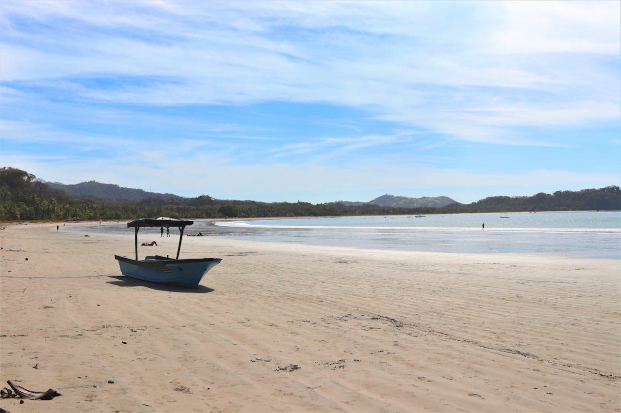 Wide sandy beach with a small fishing boat on the shore, distant mountains, and clear blue sky, capturing the tranquil and natural beauty of Costa Rica’s Pacific coast.