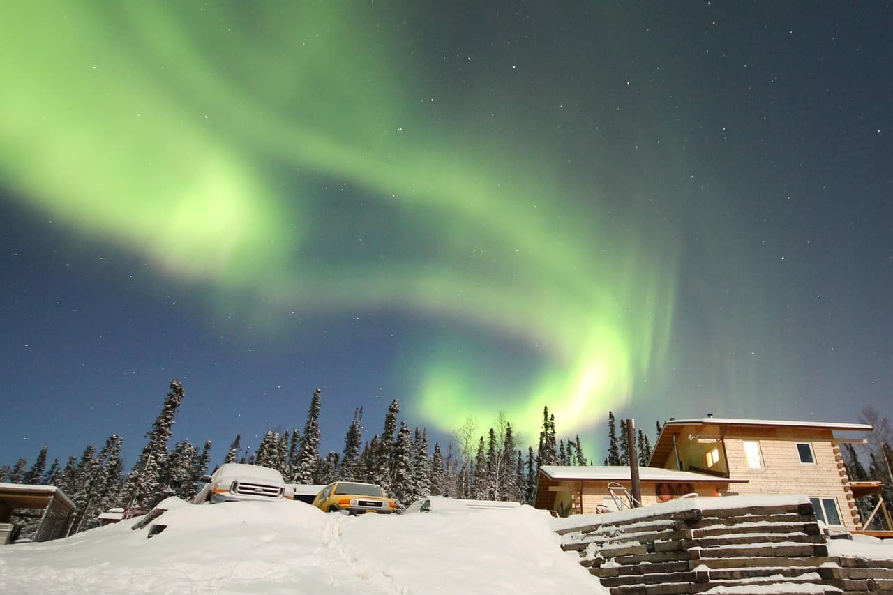 Green northern lights over snow-covered cabins in Alaska