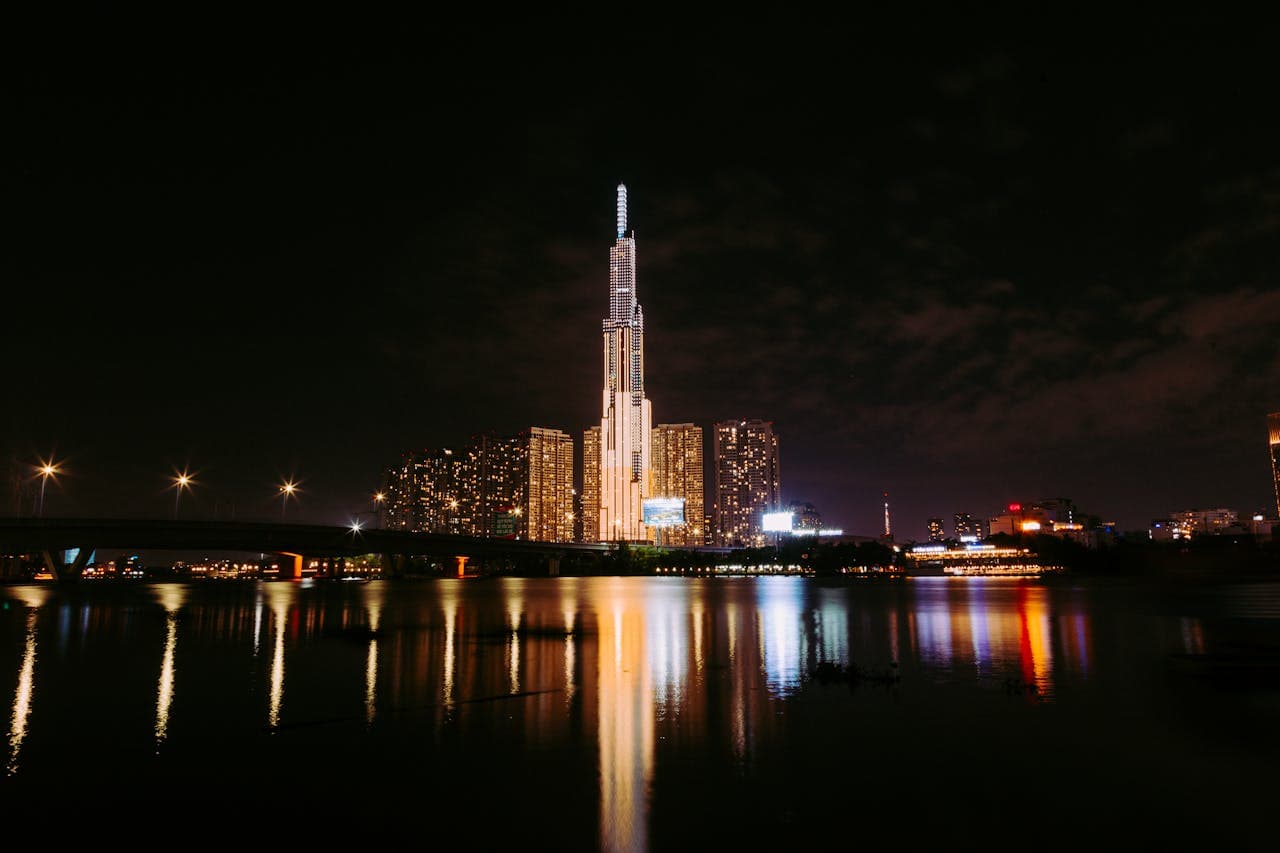Night view of Landmark 81 skyscraper in Ho Chi Minh City, Vietnam, illuminated against the dark sky with reflections shimmering on the Saigon River