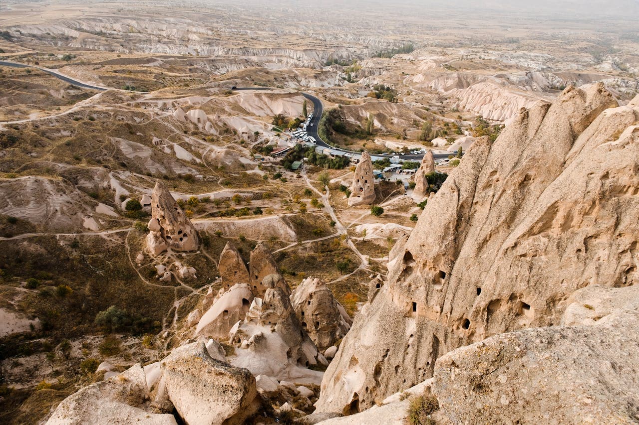 Aerial view of Cappadocia's unique rock formations and valleys, with scattered roads and sparse vegetation under a hazy sky.